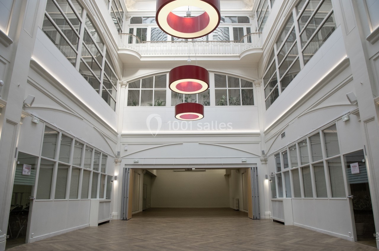 Vue intérieure d'une grande salle lumineuse avec parquet, verrière et suspensions rouges circulaires.