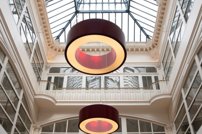 Vue intérieure d'une galerie lumineuse avec verrière, murs blancs et suspensions circulaires rouges.