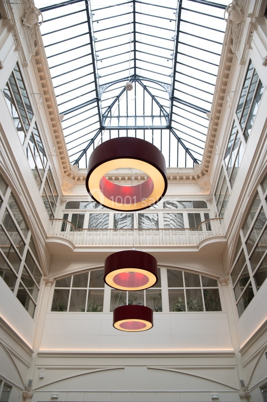 Plafond vitré d'une galerie lumineuse avec trois grands luminaires circulaires suspendus.