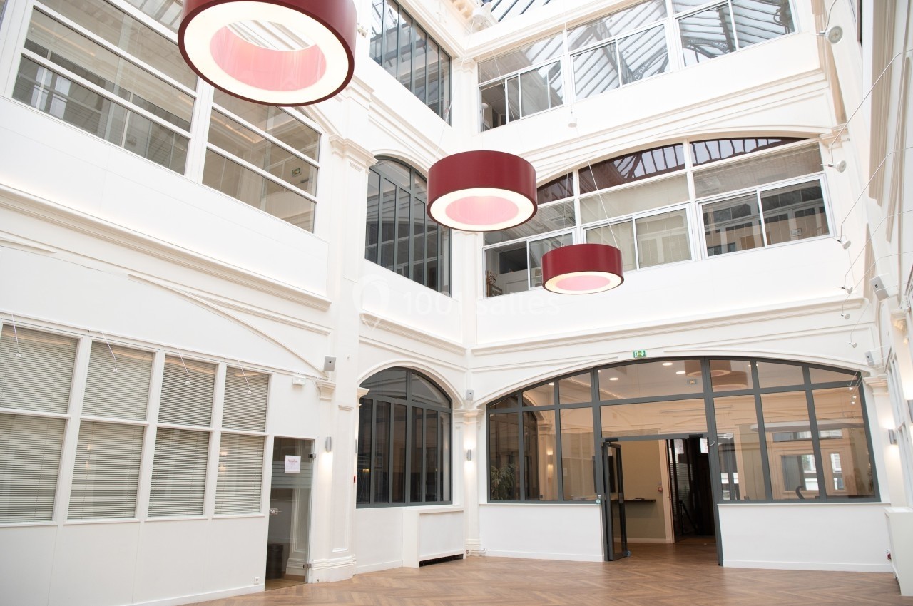 Intérieur lumineux d'un bâtiment moderne avec verrière, grandes fenêtres et suspensions circulaires rouges.