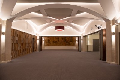 Vue intérieure d'une galerie lumineuse avec verrière, murs blancs et suspensions circulaires rouges.