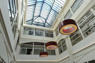 Vue intérieure d'une galerie lumineuse avec verrière, murs blancs et suspensions circulaires rouges.