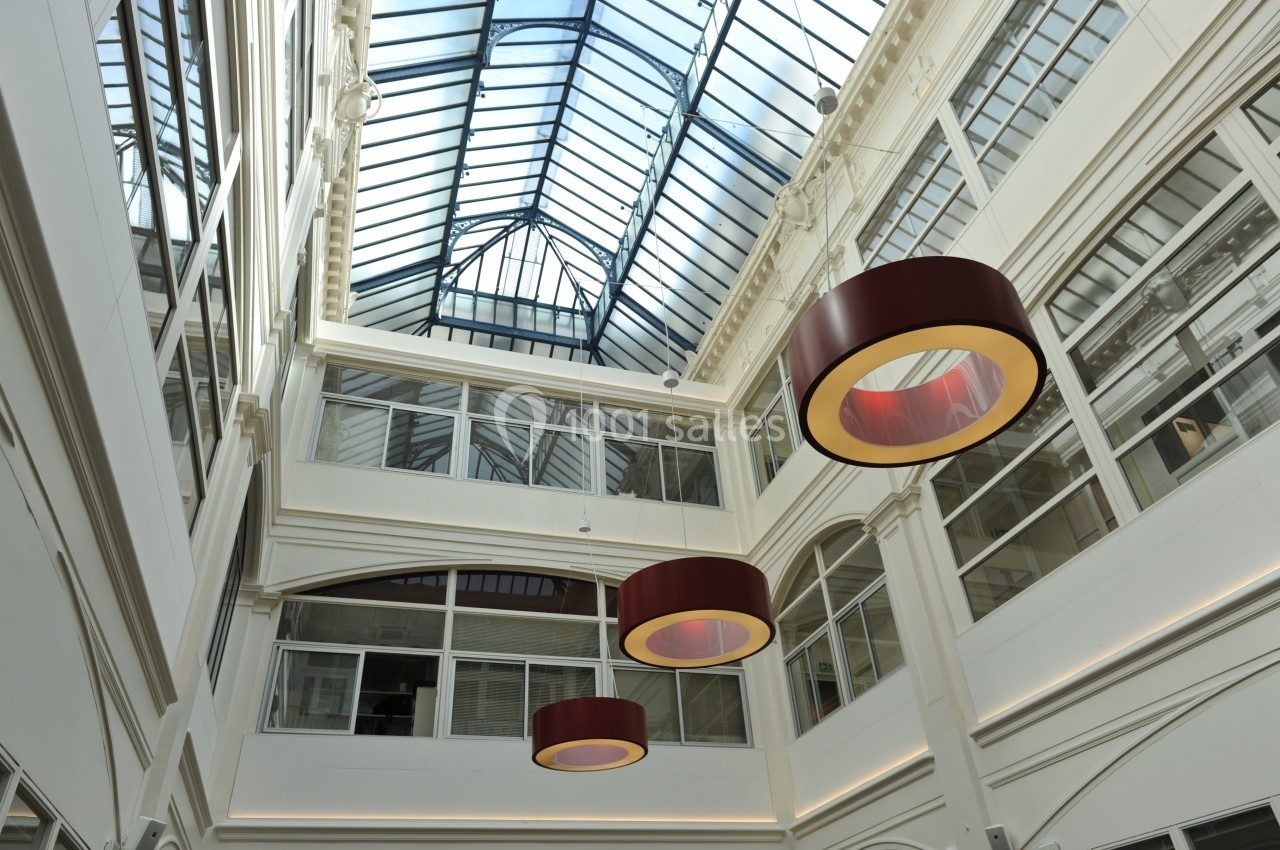 Vue intérieure d'une galerie lumineuse avec verrière, murs blancs et suspensions circulaires rouges.