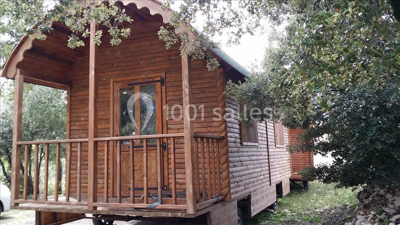 Roulotte en bois avec terrasse, entourée de végétation et située dans un environnement naturel.