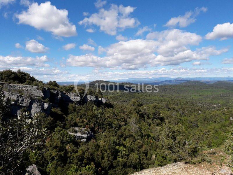 Paysage de collines boisées avec des falaises rocheuses sous un ciel bleu parsemé de nuages.