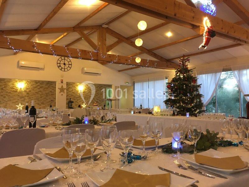 Salle décorée pour un repas festif avec tables dressées, sapin de Noël illuminé et guirlandes suspendues.