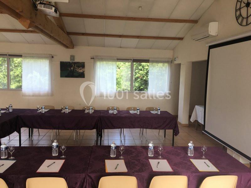 Salle de réunion lumineuse avec tables disposées en U, nappes violettes, bouteilles d'eau, verres et bloc-notes.