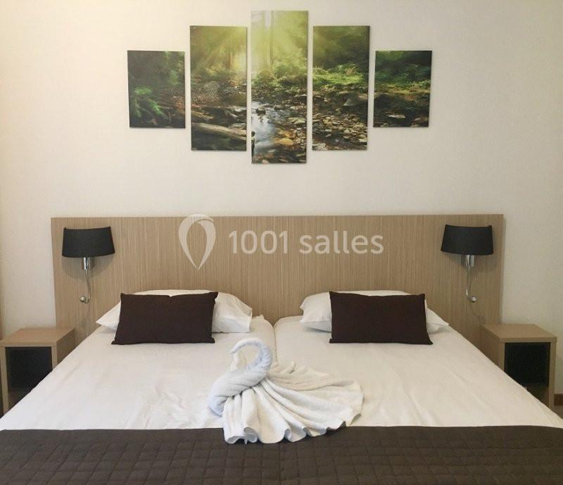 Lit double avec tête de lit en bois, deux lampes de chevet, et décoration murale représentant une forêt.