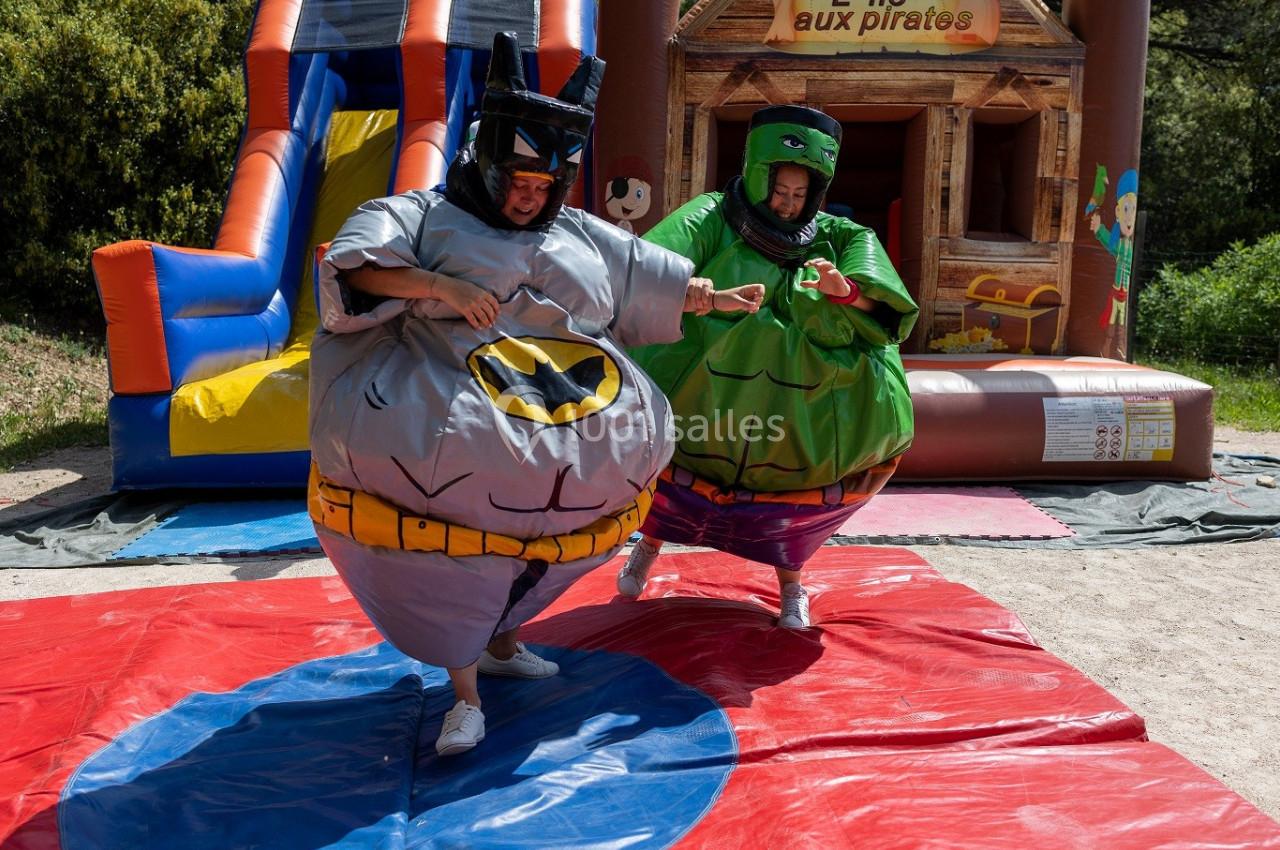 Deux personnes déguisées en costumes gonflables s'affrontent sur un tapis devant une structure gonflable.