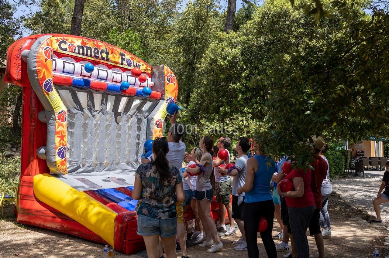 Des personnes jouent à un jeu gonflable coloré en plein air, entourées d'arbres et de lumière naturelle.