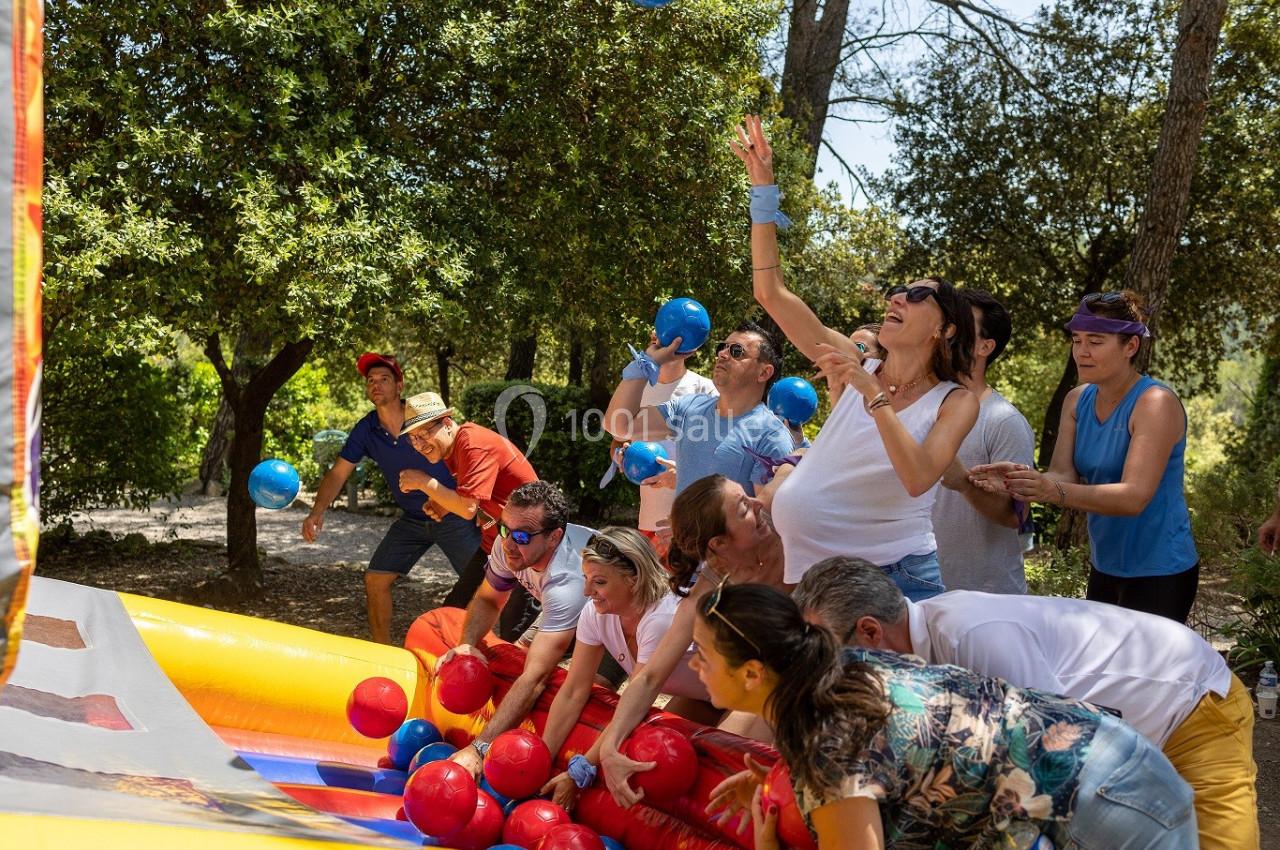 Des personnes participent à un jeu collectif en extérieur, lançant des balles colorées dans un cadre boisé.