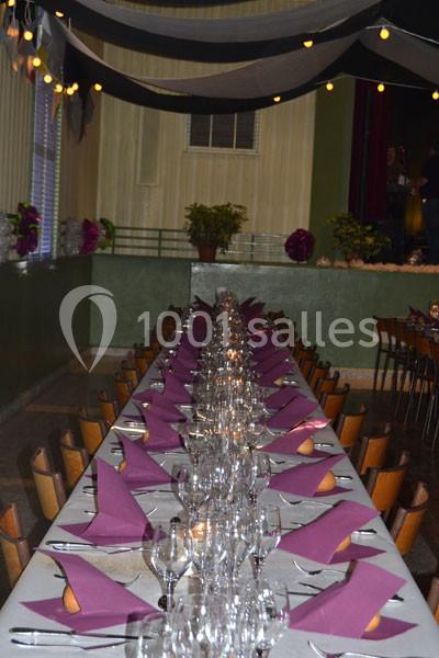 Table dressée pour un repas, avec nappes blanches, serviettes violettes pliées et verres alignés sous une décoration…