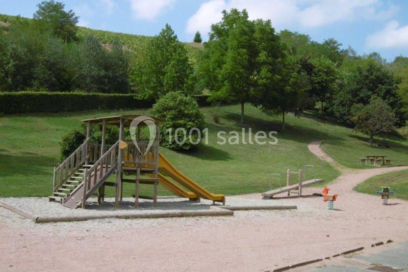 Aire de jeux extérieure avec toboggan, balançoires et structures en bois, entourée de pelouse et d'arbres.
