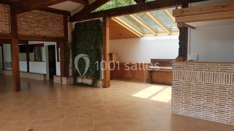 Salle lumineuse avec murs en briques, sol en carrelage, plafond en bois, verrière et un piano en arrière-plan.