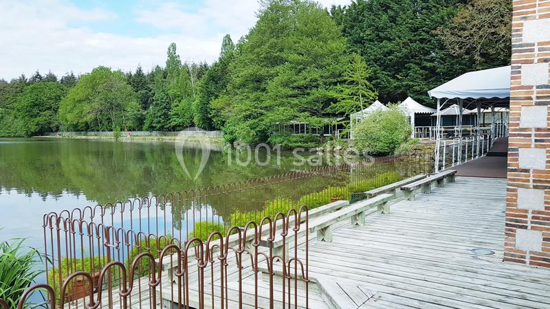 Passerelle en bois bordant un étang entouré de végétation et de tentes blanches près d'un bâtiment en briques.