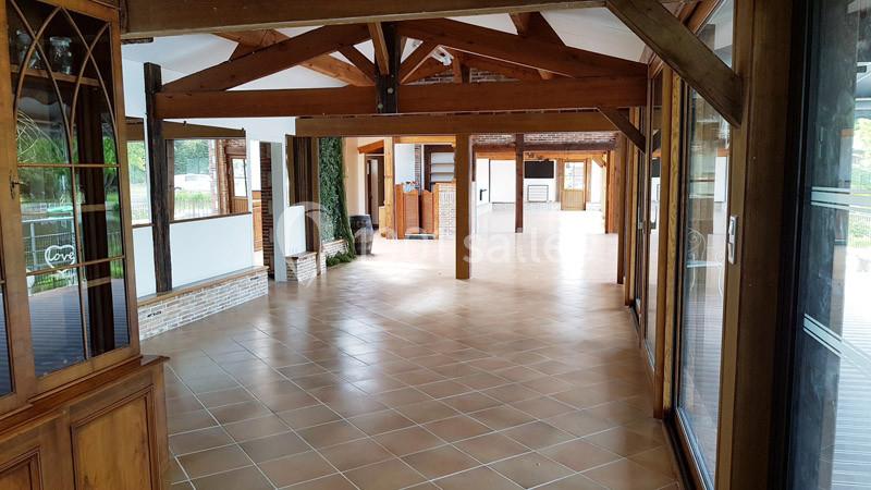 Intérieur spacieux avec poutres en bois apparentes, carrelage au sol et grandes ouvertures vitrées.