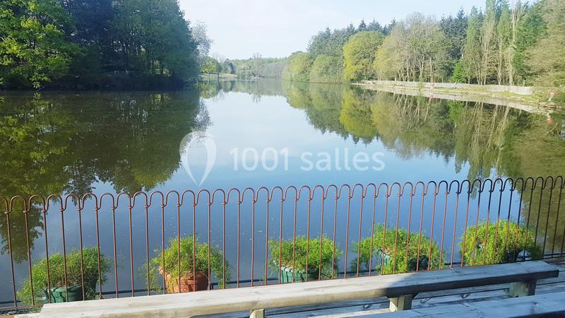 Vue d'un étang entouré d'arbres, avec une barrière en métal et des jardinières au premier plan.