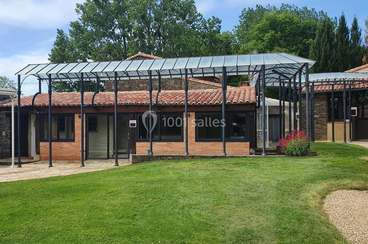 Bâtiment avec toit en verre, murs en briques et jardin verdoyant, entouré d'arbres et d'allées pavées.