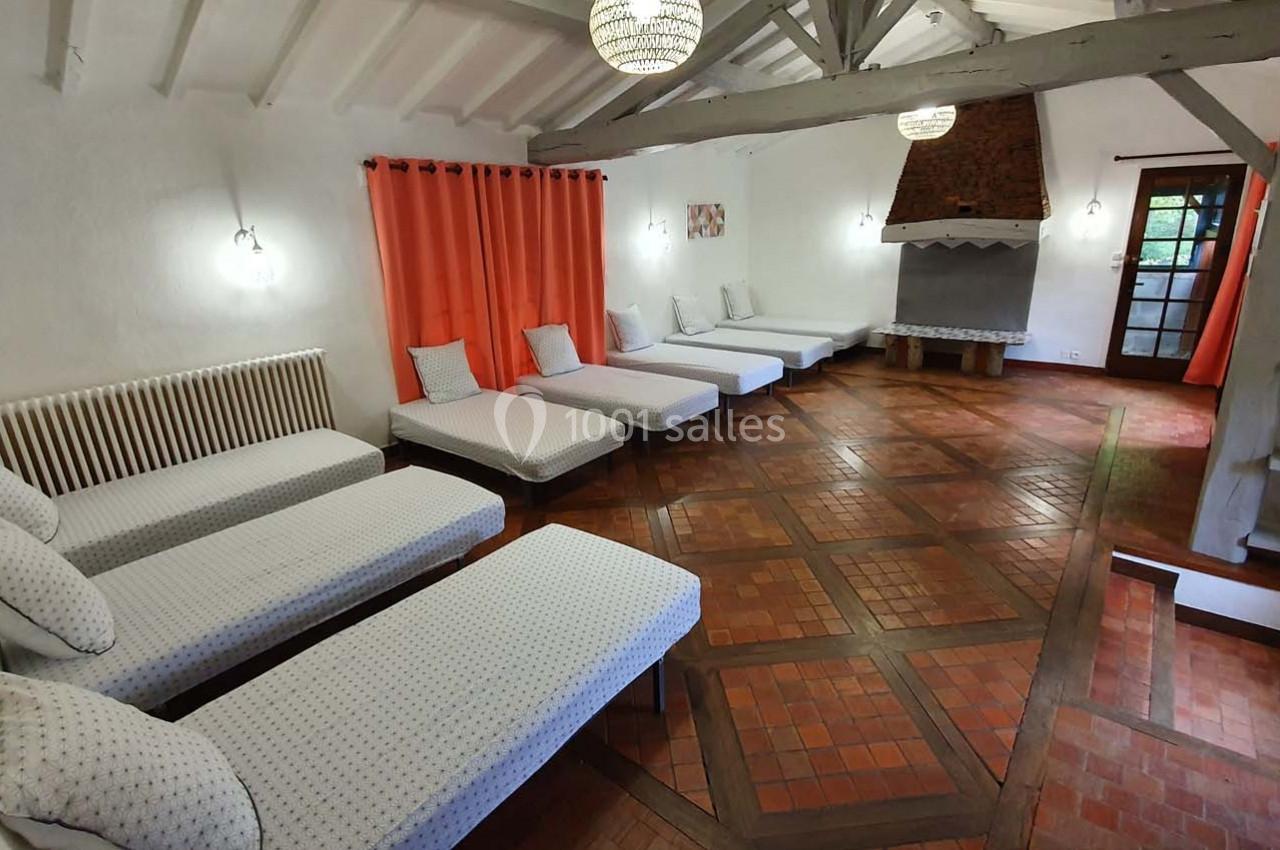 Salle avec plusieurs lits simples alignés, parquet en bois, cheminée en briques et rideaux rouges.