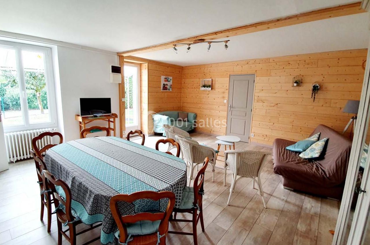 Salle à manger et salon lumineux avec murs en bois, table rectangulaire, chaises, canapé et vue sur un jardin.