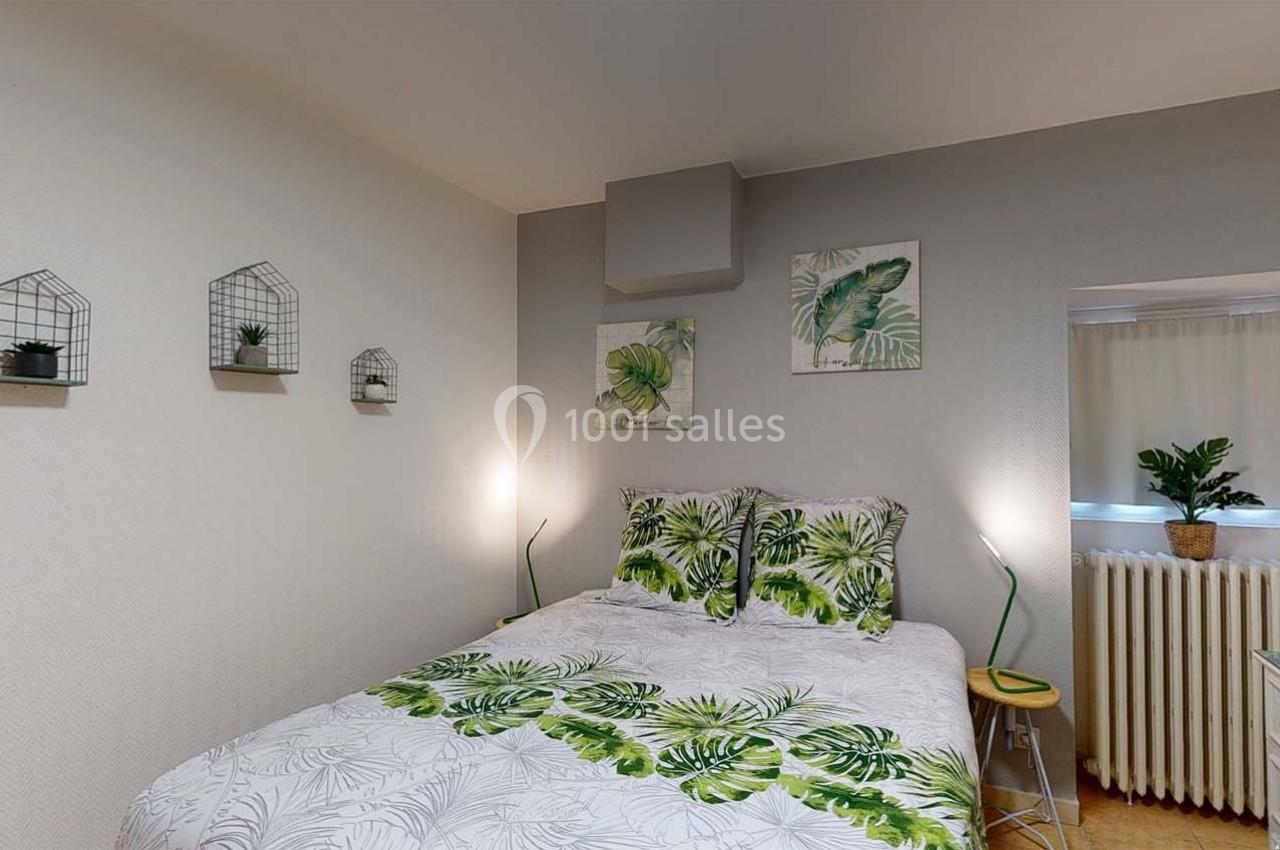 Chambre lumineuse avec lit double, linge à motif tropical, décorations murales et petite plante près d'une fenêtre.