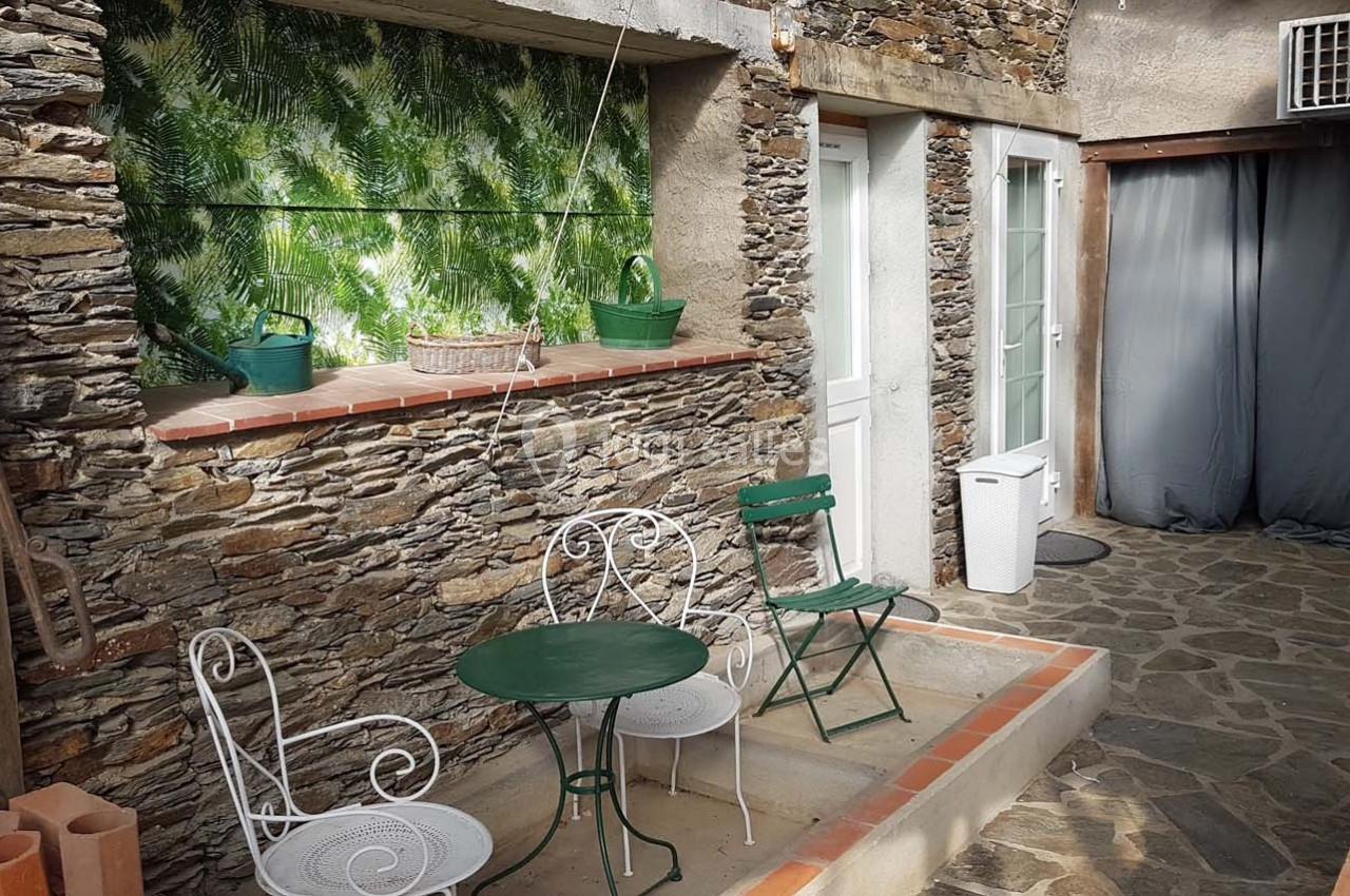 Petite cour en pierre avec mobilier de jardin en métal, mur en pierre, plantes et porte blanche.