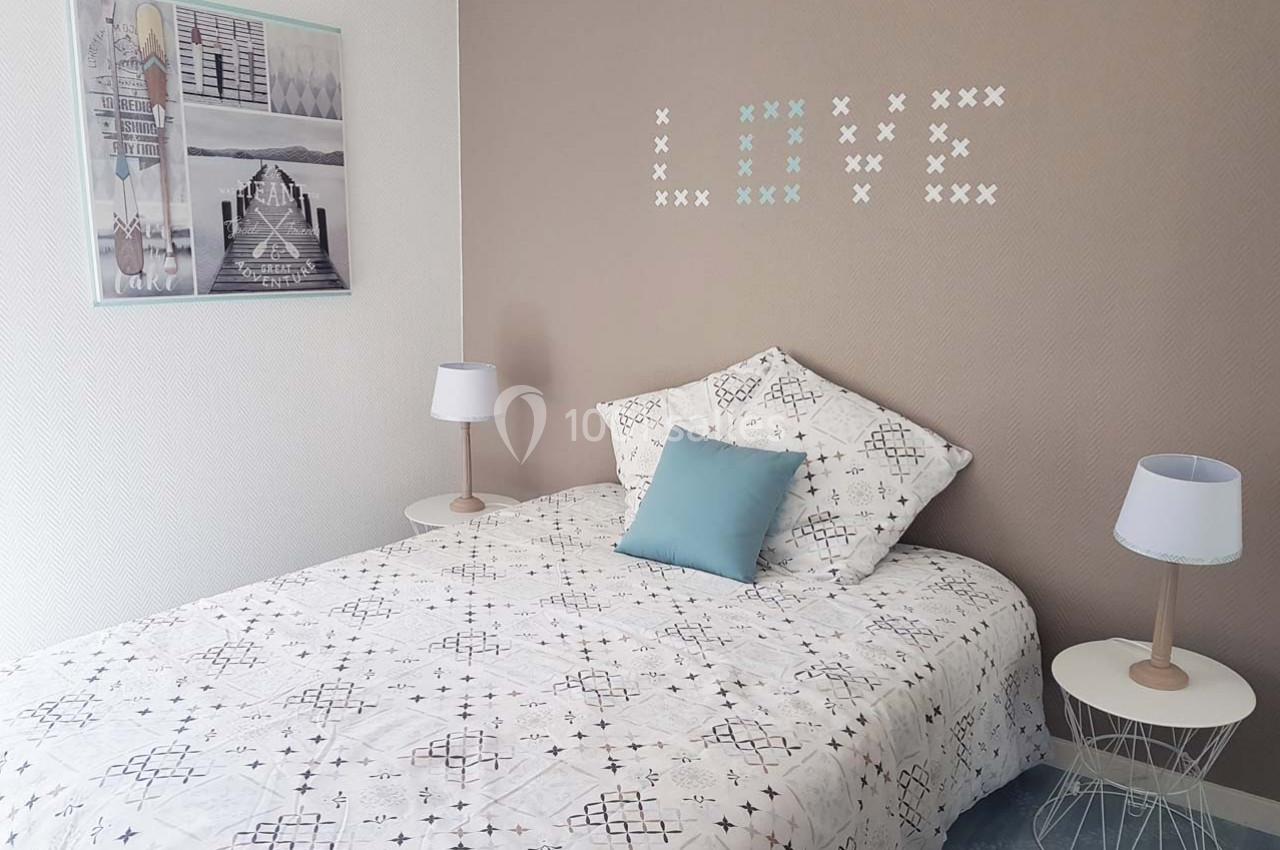 Chambre lumineuse avec un lit simple, une décoration murale ’LOVE’ et deux tables de chevet avec lampes.
