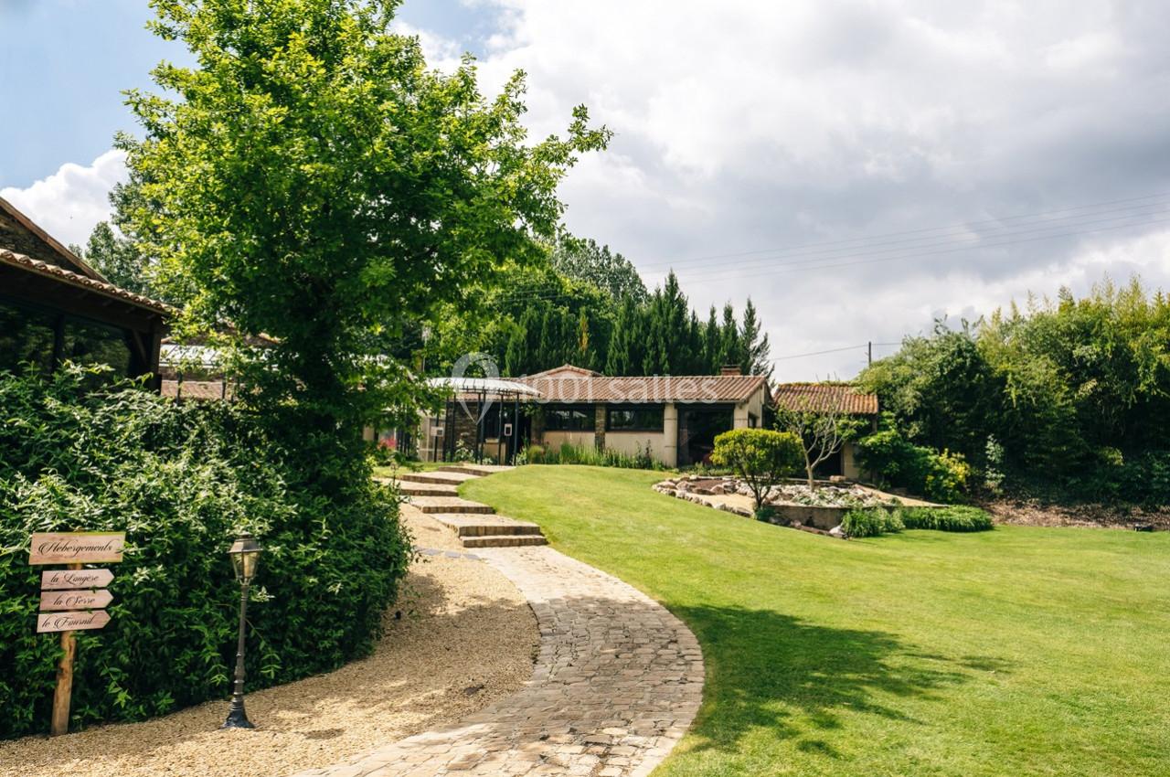 Allée pavée menant à des bâtiments entourés de verdure et d'arbres sous un ciel partiellement nuageux.