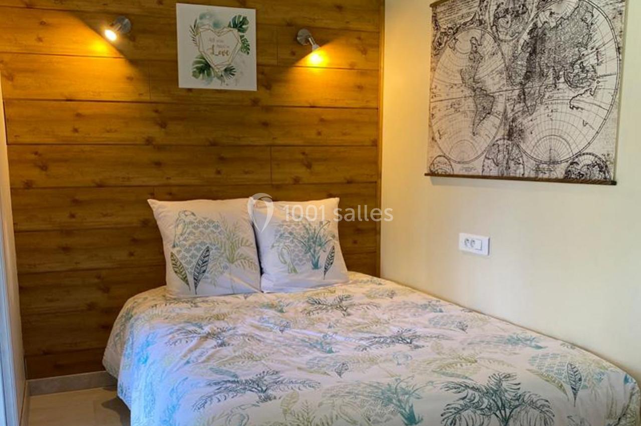 Lit double avec housse de couette à motifs végétaux, éclairé par deux appliques murales sur un mur en bois clair.