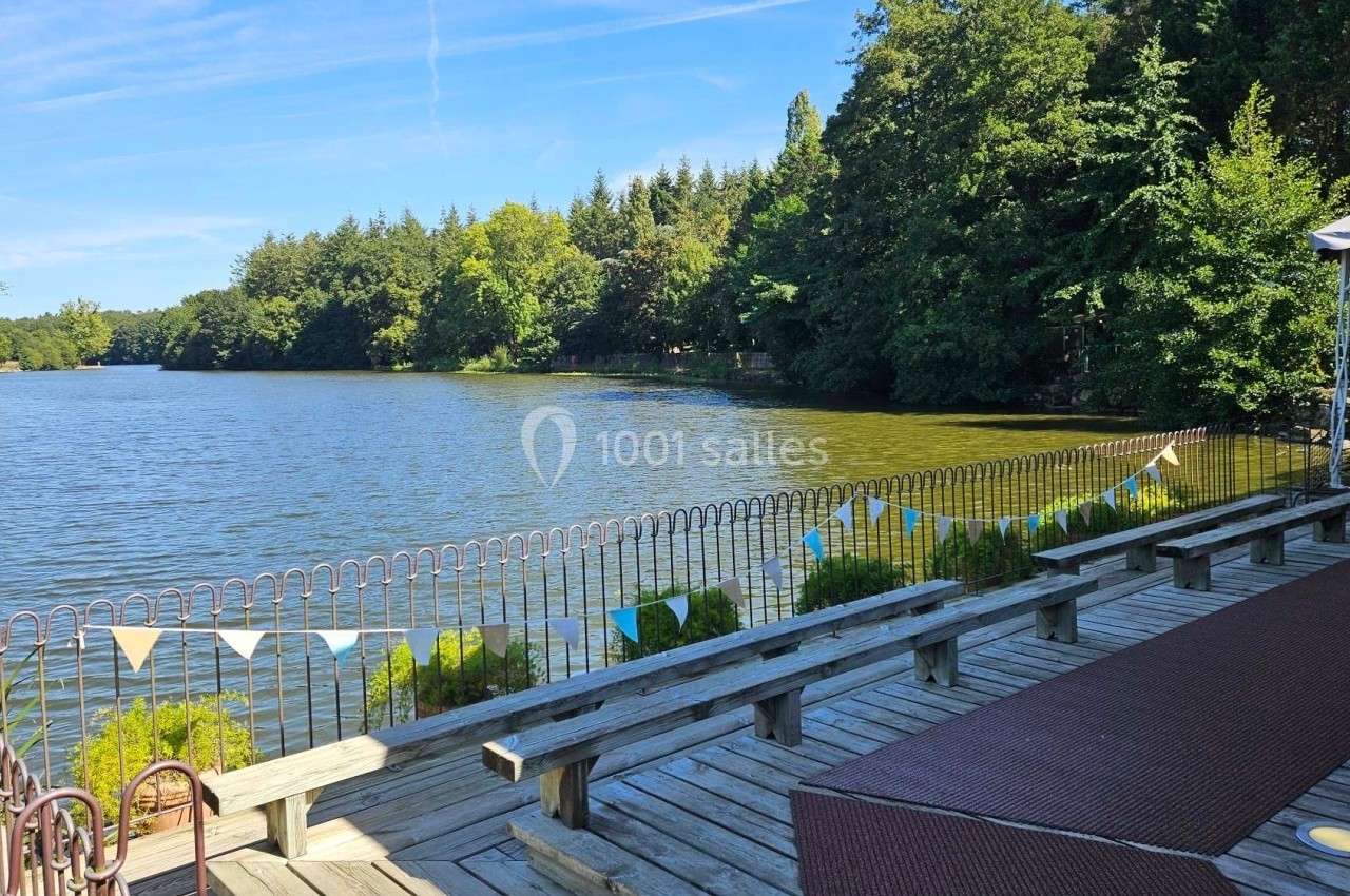 Vue d'un lac bordé d'arbres, avec une terrasse en bois et une rambarde décorée de fanions colorés au premier plan.