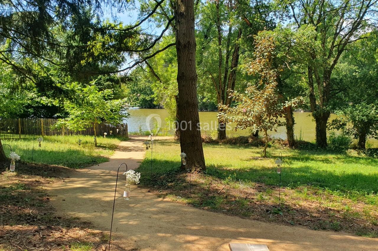 Chemin en terre bordé d'arbres menant à un plan d'eau entouré de végétation.