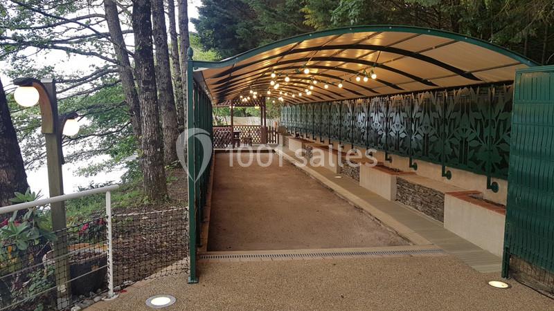 Abri couvert en bois et métal avec bancs, situé en extérieur près d'arbres et d'un plan d'eau.