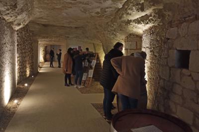 Bâtiment moderne éclairé la nuit, entouré d'un espace extérieur sombre avec un ciel nuageux en arrière-plan.