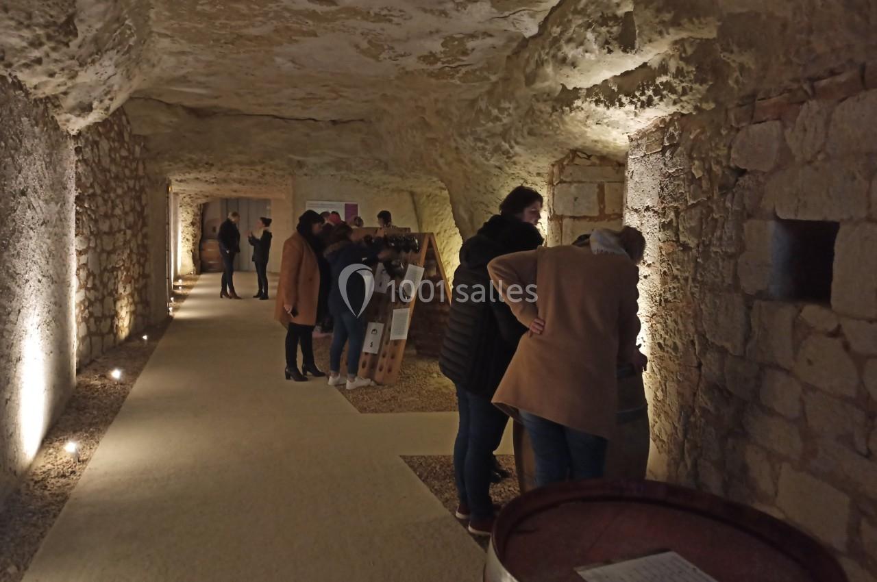 Visiteurs observant des panneaux explicatifs dans une galerie souterraine éclairée, aux murs en pierre.