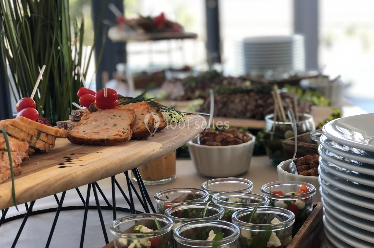 Buffet avec des plats variés, incluant des verrines, du pain, des légumes et des assiettes empilées en arrière-plan.