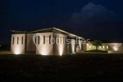 Bâtiment moderne éclairé la nuit, entouré d'un espace extérieur sombre avec un ciel nuageux en arrière-plan.