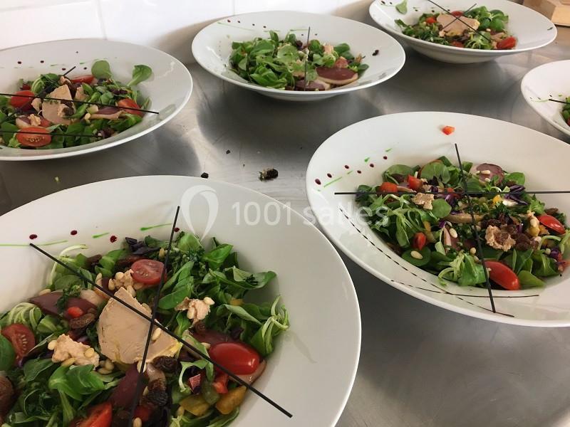 Assiettes de salades composées avec tomates cerises, noix, foie gras et légumes, disposées sur une table en inox.
