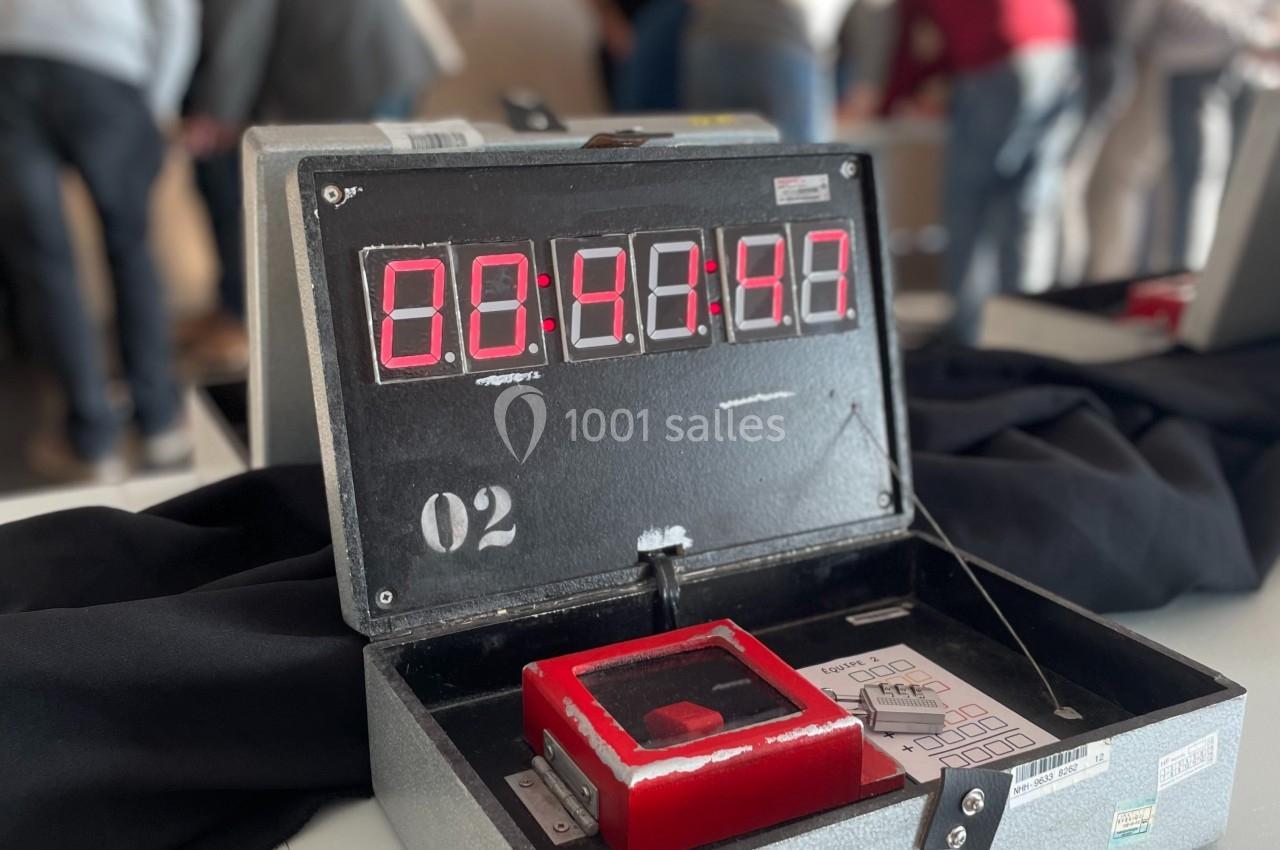 Boîtier métallique ouvert avec un chronomètre numérique affichant 00:40:00, entouré de personnes en arrière-plan.