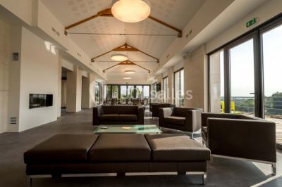 Bâtiment moderne éclairé la nuit, entouré d'un espace extérieur sombre avec un ciel nuageux en arrière-plan.