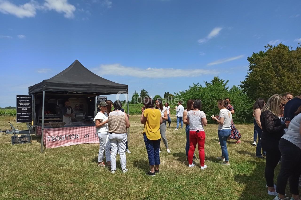 Groupe de personnes rassemblées devant un stand alimentaire sous une tente noire dans un espace extérieur verdoyant.