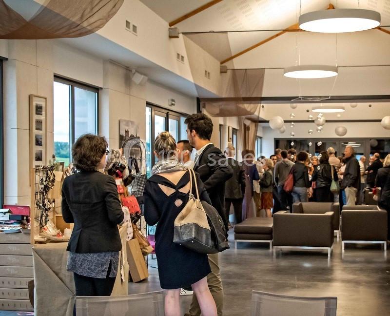 Des personnes discutent et observent des stands dans une salle lumineuse lors d'un événement ou d'une exposition.