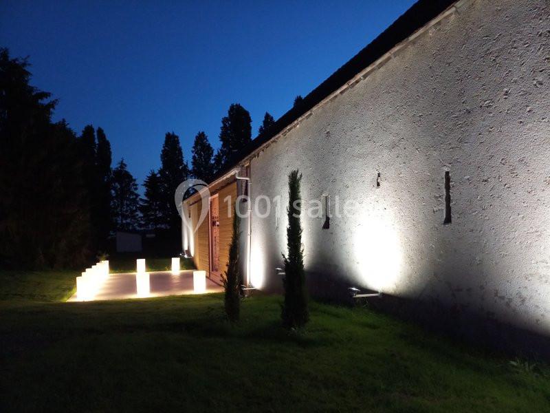 Façade d'un bâtiment éclairée par des lumières au sol, avec un chemin illuminé et des arbres en arrière-plan.