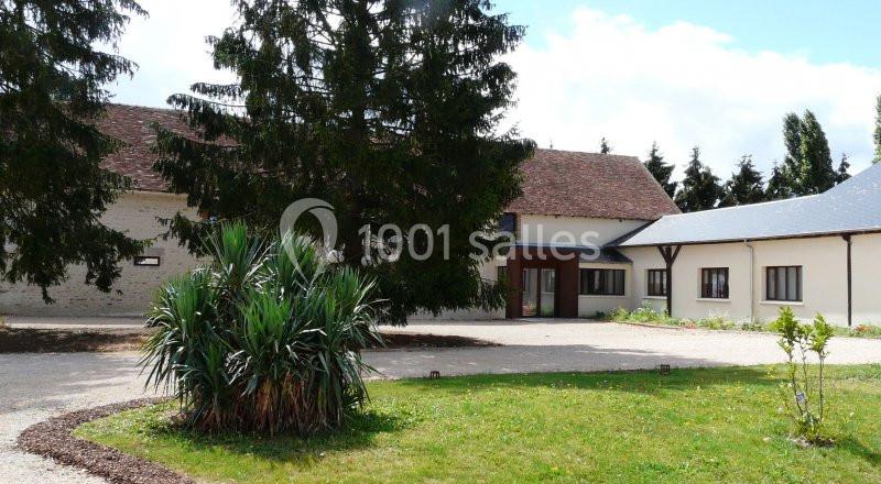 Bâtiment rural avec toit en tuiles, entouré d'arbres, d'une pelouse et d'une allée gravillonnée.