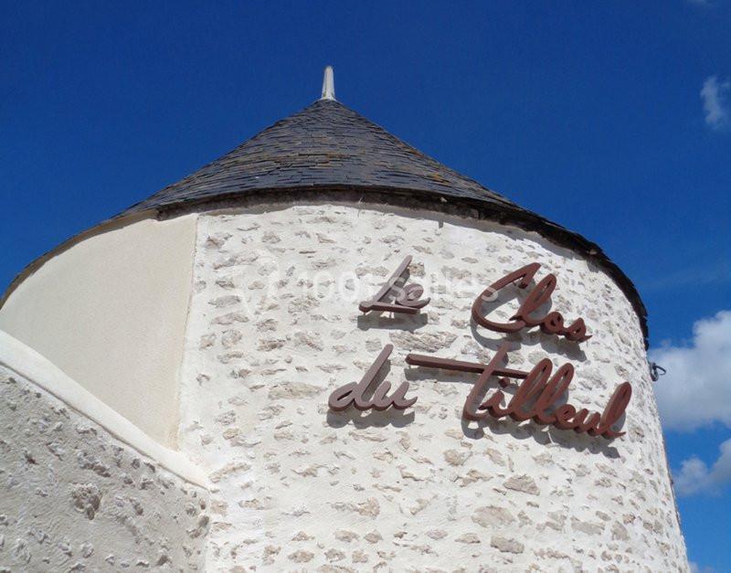 Mur en pierre blanche avec une inscription ’Le Clos du Tilleul’ et un toit conique sous un ciel bleu.