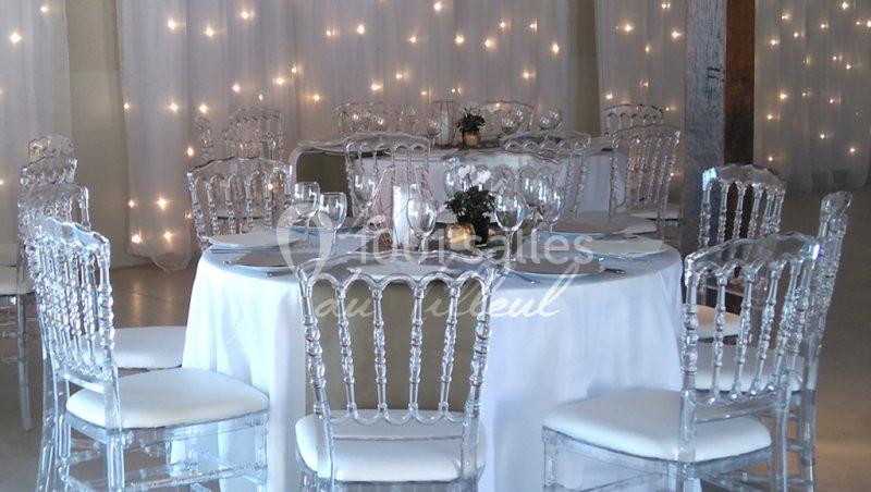 Table ronde décorée avec une nappe blanche, chaises transparentes et guirlandes lumineuses en arrière-plan.