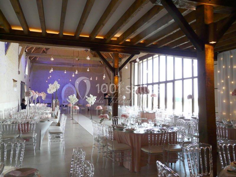 Salle de réception élégante avec tables dressées, chaises transparentes et décorations florales dans un cadre lumineux.