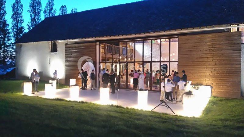 Groupe de personnes rassemblées en soirée devant un bâtiment moderne éclairé, avec des lampes décoratives au sol.