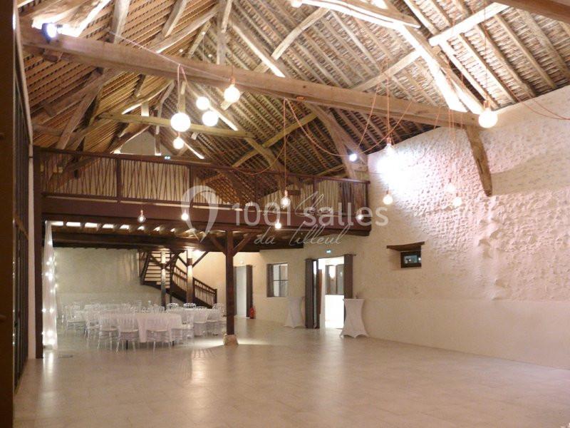 Salle de réception spacieuse avec charpente en bois apparente, tables dressées et éclairage suspendu.