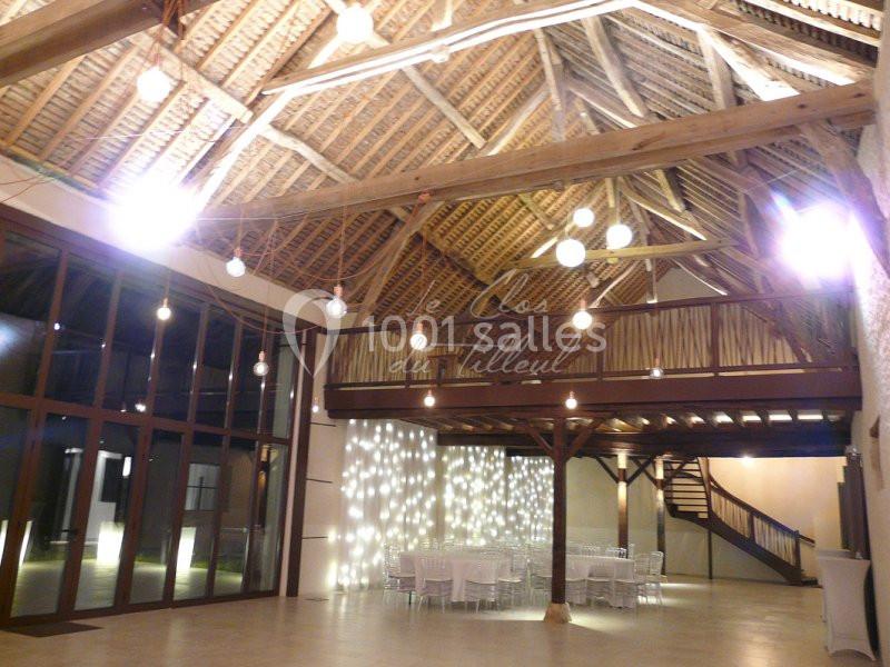 Intérieur d'une salle de réception avec charpente en bois apparente, tables dressées et éclairage suspendu.