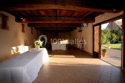 Chambre lumineuse avec poutres apparentes, lit double, table blanche, et vue sur un balcon avec verdure.